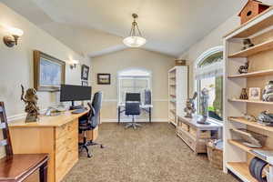 Home office with lofted ceiling, plenty of natural light, and light colored carpet