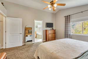 Carpeted bedroom with baseboards, lofted ceiling, ceiling fan, and ensuite bathroom
