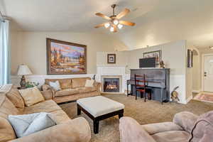 Living area featuring a fireplace with flush hearth, lofted ceiling, a ceiling fan, wainscoting, and carpet flooring
