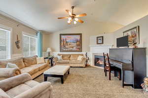 Living room with a fireplace with flush hearth, vaulted ceiling, carpet floors, wainscoting, and ceiling fan