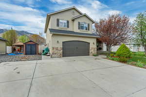 Traditional-style home with concrete driveway, stone siding, an attached garage, stucco siding, and a storage unit