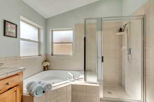 Bathroom featuring a shower stall, vaulted ceiling, vanity, and a garden tub
