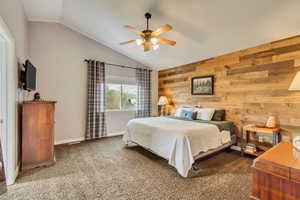 Bedroom with vaulted ceiling, carpet flooring, wood walls, and a ceiling fan