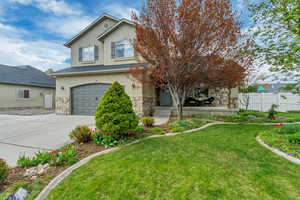 View of front of house featuring an attached garage, driveway, stone siding, and fence