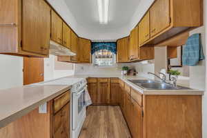 Kitchen with a sink, light wood-style floors, light countertops, under cabinet range hood, and white electric stove