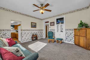 Living area with wallpapered walls, a wainscoted wall, carpet, and ceiling fan