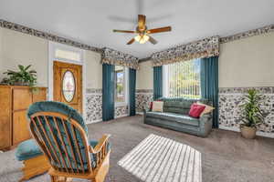 Carpeted living room with wainscoting, a ceiling fan, and wallpapered walls
