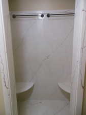 Master bathroom featuring a marble finish double shower with two shower seats.