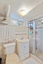 Three-quarter bath with tile patterned floors, toilet, vanity, tile walls, and a walk-in shower