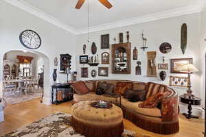 Large living area featuring ceiling fan, arched doorway, crown molding, and light hardwood finished floors