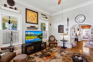 Living room with arched doorway, plantation shutters, ornamental crown molding, hardwood floors, and lots of natural sunlight