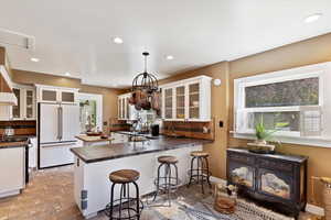 Tastefully updated kitchen featuring white cabinets with glass, recessed lighting, dark Dekton countertops, and a peninsula