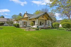 View of front Craftsman-style home with 3-tone painted brick / cedar shake shingles, lush green lawn.