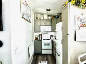 Kitchen with a textured ceiling, white appliances, lofted ceiling, dark wood-style flooring, and gray cabinetry
