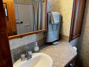 Bathroom with vanity, curtained shower, and wallpapered walls