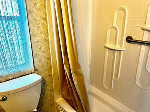 Bathroom with wallpapered walls, curtained shower, and toilet