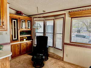Living area with crown molding, a textured ceiling, a wainscoted wall, light colored carpet, and wood walls