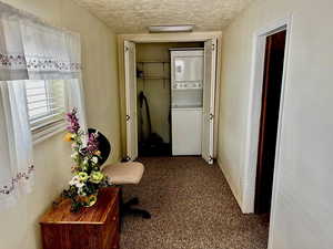 Corridor with baseboards, carpet floors, stacked washer and clothes dryer, and a textured ceiling