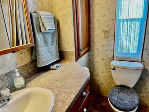 Bathroom featuring toilet, vanity, and wallpapered walls