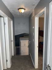 Corridor featuring visible vents, carpet flooring, a textured ceiling, and an upstairs landing