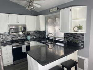 Kitchen with a sink, decorative backsplash, ceiling fan, stainless steel appliances, and a peninsula