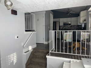Stairs featuring wood finished floors, a ceiling fan, baseboards, and a textured ceiling