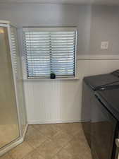 Laundry room with light tile patterned floors, a wainscoted wall, laundry area, and independent washer and dryer