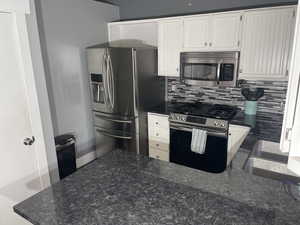 Kitchen featuring decorative backsplash, dark stone countertops, stainless steel appliances, and white cabinets