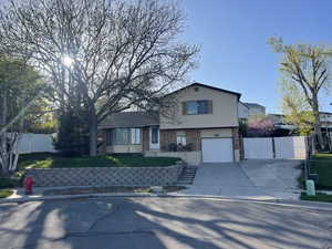 Tri-level home featuring a garage, driveway, fence, a front yard, and brick siding facing west