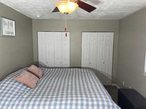 Bedroom with a ceiling fan, multiple closets, a textured ceiling, and carpet