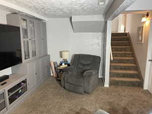 Basement living area featuring a textured ceiling, stairway, visible vents, and carpet floors