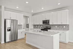Kitchen with appliances with stainless steel finishes, a sink, light wood-style floors, white cabinetry, and tasteful backsplash