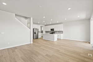 Unfurnished living room with recessed lighting, light wood-style flooring, baseboards, and stairs