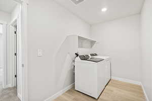 Washroom featuring washer and clothes dryer, baseboards, and light wood-type flooring