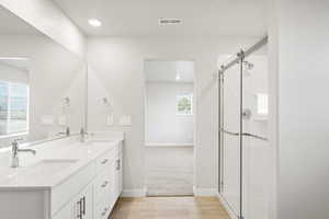 Bathroom featuring double vanity, a tile shower, wood finished floors, baseboards, and recessed lighting