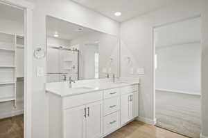 Full bathroom featuring a spacious closet, double vanity, a shower stall, baseboards, and recessed lighting
