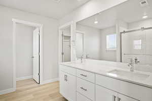 Full bathroom featuring double vanity, wood finished floors, a shower stall, baseboards, and recessed lighting