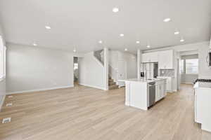 Kitchen with appliances with stainless steel finishes, white cabinetry, light wood-style floors, an island with sink, and light countertops