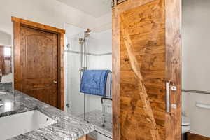 En-suite bathroom featuring glass enclosed tile shower, 2 private toilet rooms, dual sinks, granite countertops and glass medicine cabinet