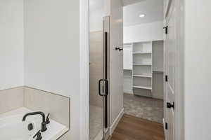 Bathroom featuring recessed lighting, a spacious closet, wood finished floors, a shower stall, and a garden tub