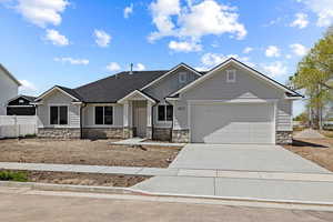 View of front of house with fence, board and batten siding, driveway, stone siding, and a garage
