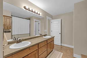 Full bathroom with baseboards, tile patterned flooring, a sink, and double vanity