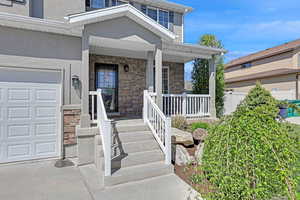 Doorway to property with stone siding, a porch, stucco siding, and a garage