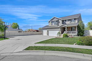 Traditional home with concrete driveway, stone siding, fence, a porch, and a front yard