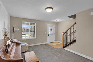 Entrance foyer with baseboards, carpet floors, a textured ceiling, and stairs