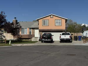 Tri-level home with a garage, fence, a chimney, brick siding, and concrete driveway