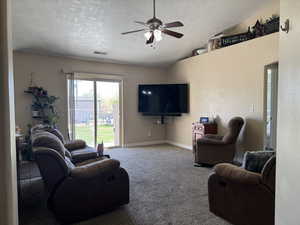 Carpeted living area with a textured ceiling, vaulted ceiling, baseboards, visible vents, and a ceiling fan