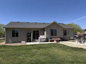 Rear view of property featuring a lawn, a shingled roof, and a patio