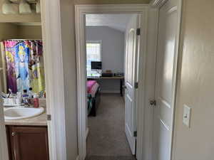 Hallway featuring carpet, vaulted ceiling, baseboards, and a sink