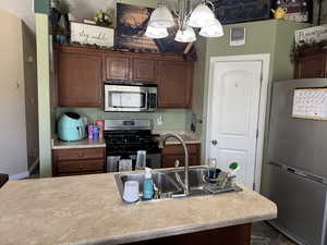 Kitchen with stainless steel appliances, a sink, baseboards, a chandelier, and light countertops